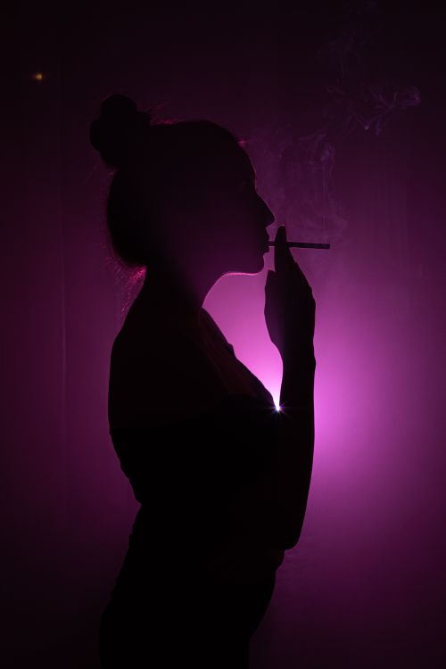 Free Artistic studio shot of a woman smoking in silhouette, highlighted by purple light. Stock Photo