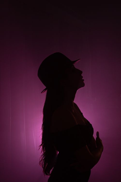 Free Artistic silhouette of a woman in a hat with dramatic backlighting and pink hues. Stock Photo