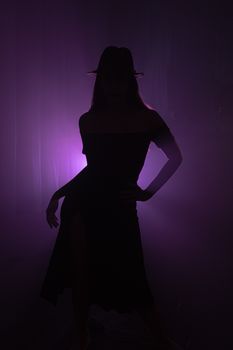 Mysterious silhouette of a woman posing in a hat against vibrant purple light, creating a dramatic effect.