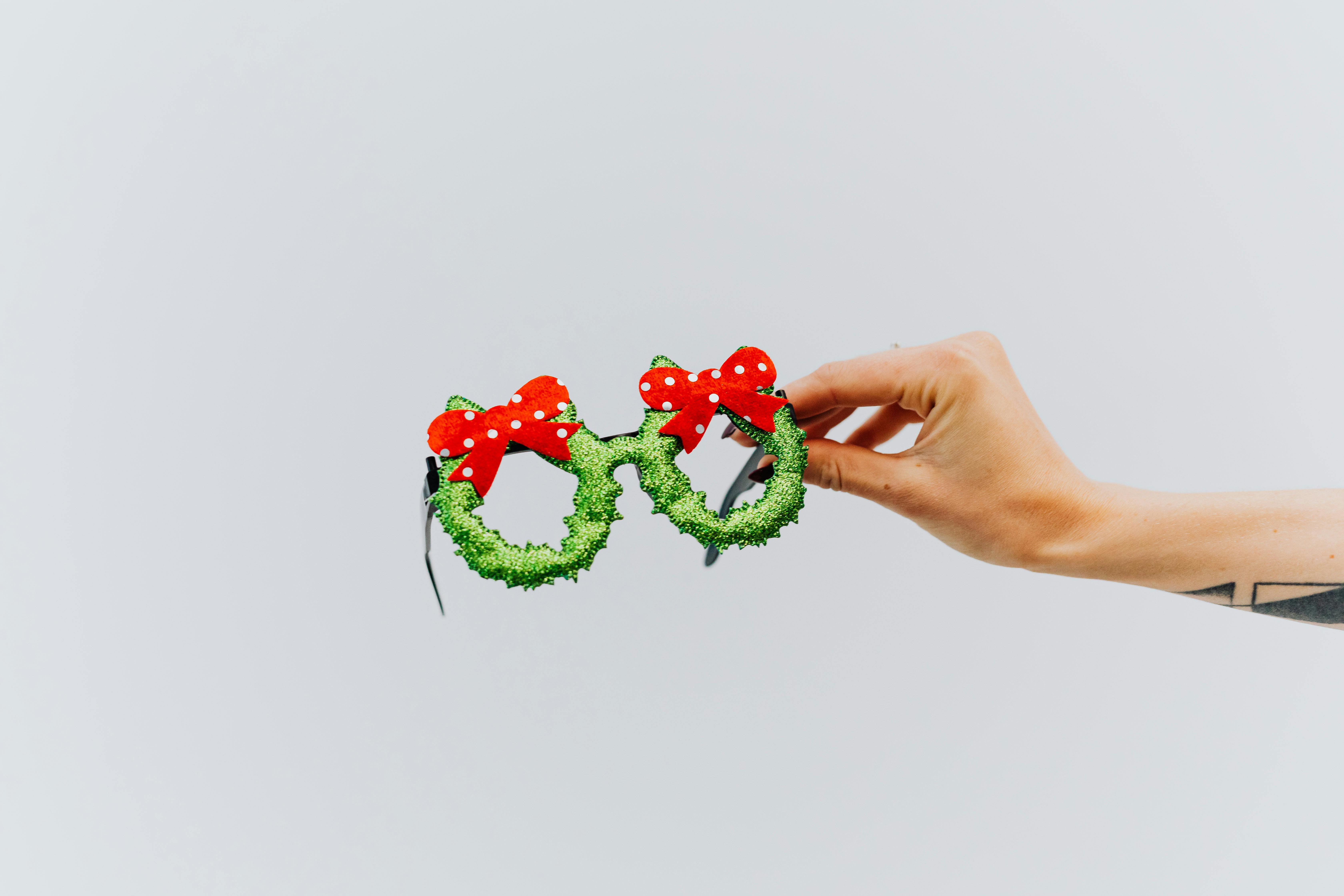 白色背景上，手持一副红色蝴蝶结的节日圣诞主题眼镜