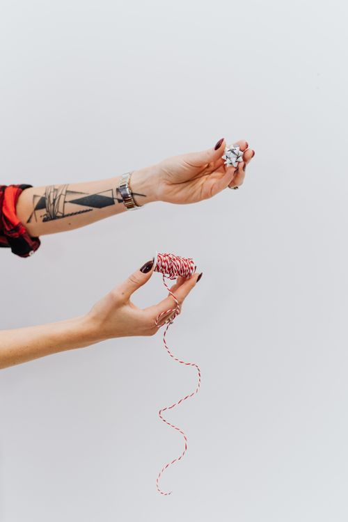 Free Tattooed hands holding and manipulating red and white yarn against a white background. Stock Photo