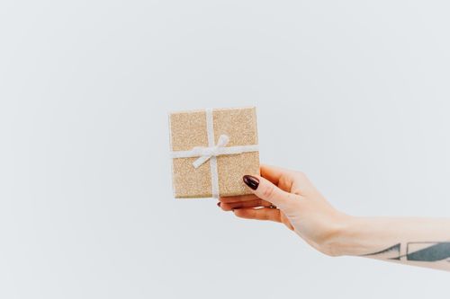 Free Close-up of a gold gift box with a white ribbon held by a tattooed hand against a white background. Stock Photo
