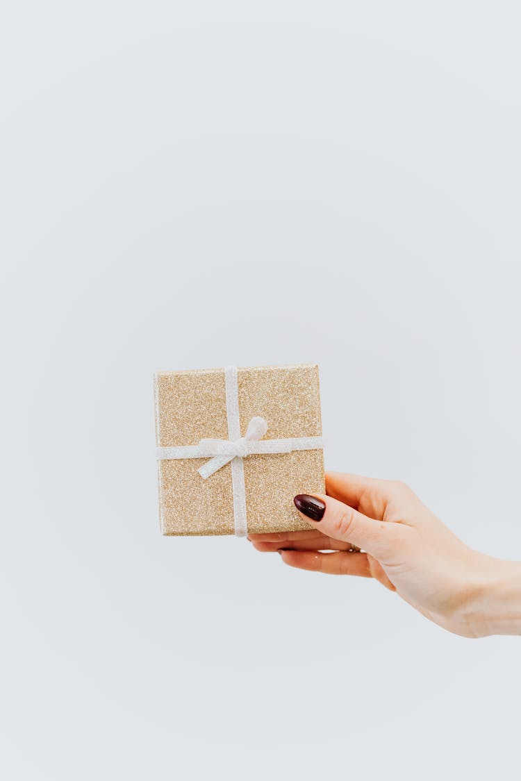 A Hand Holding A Present Wrapped With Gold Paper