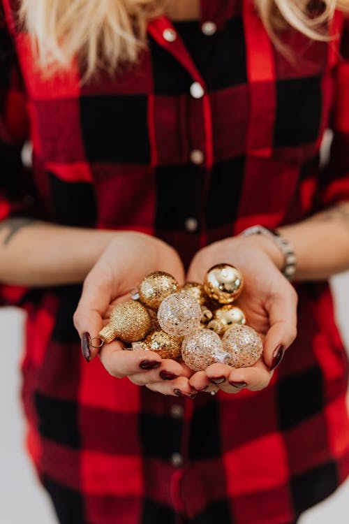 Woman in Red and Black Shirt Holding Golden Baubles