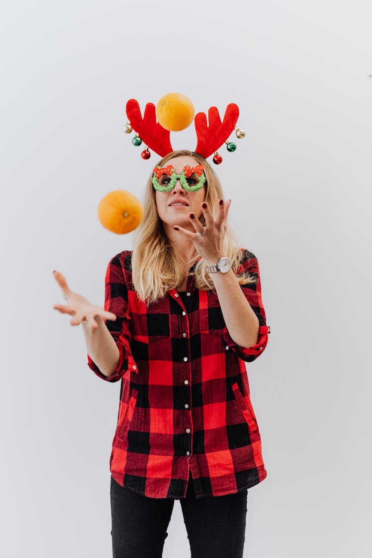 Woman In Red And Black Plaid Shirt And Christmas Horns Juggling Oranges