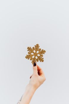 一只手持着一枚美丽的金色雪花装饰，背景是冬日景色，充满节日氛围