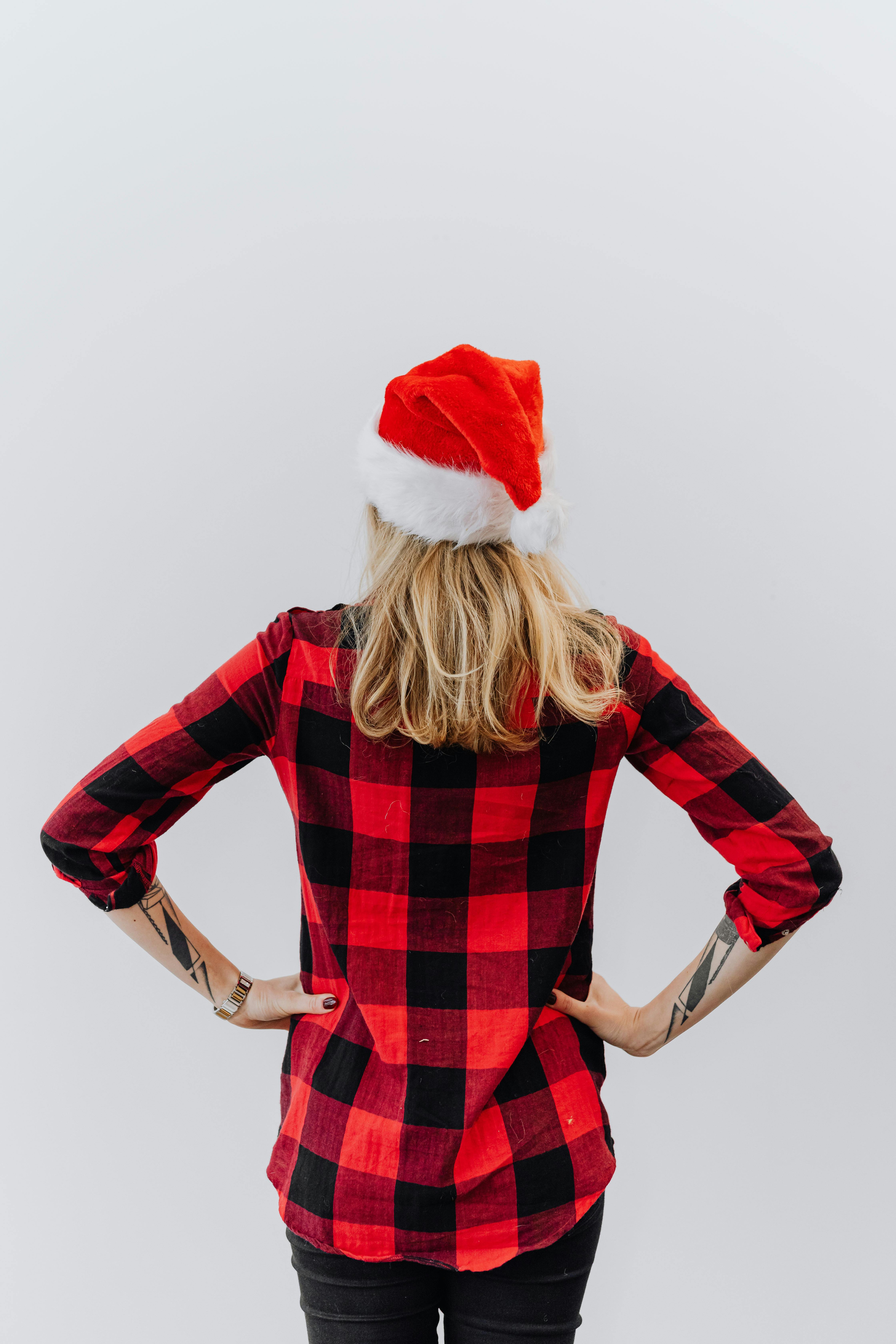 一个女人的后视图，她穿着红色格子衬衫，戴着圣诞老人帽子，手放在腰上，身上有纹身