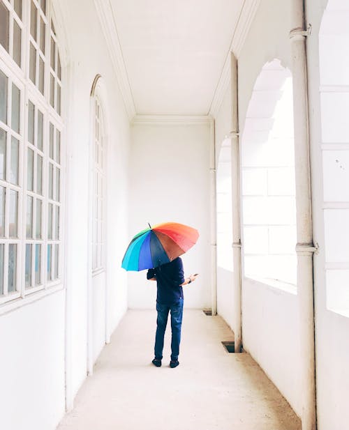 A Person Holding an Open Colorful Umbrella while Standing on a Hallway