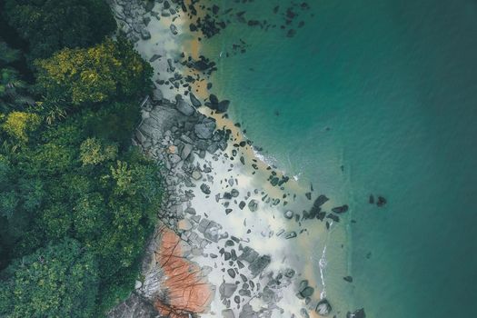 Drone view of uninhabited tropical coastline with big boulders and green trees in woods near calm sea