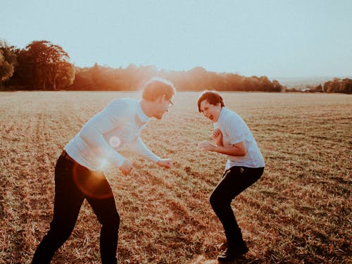 Side view of teen boy with father having fun and playing in field at sunset