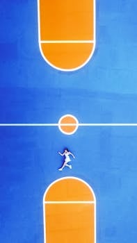 Top-down shot of a woman lying on a colorful outdoor basketball court.