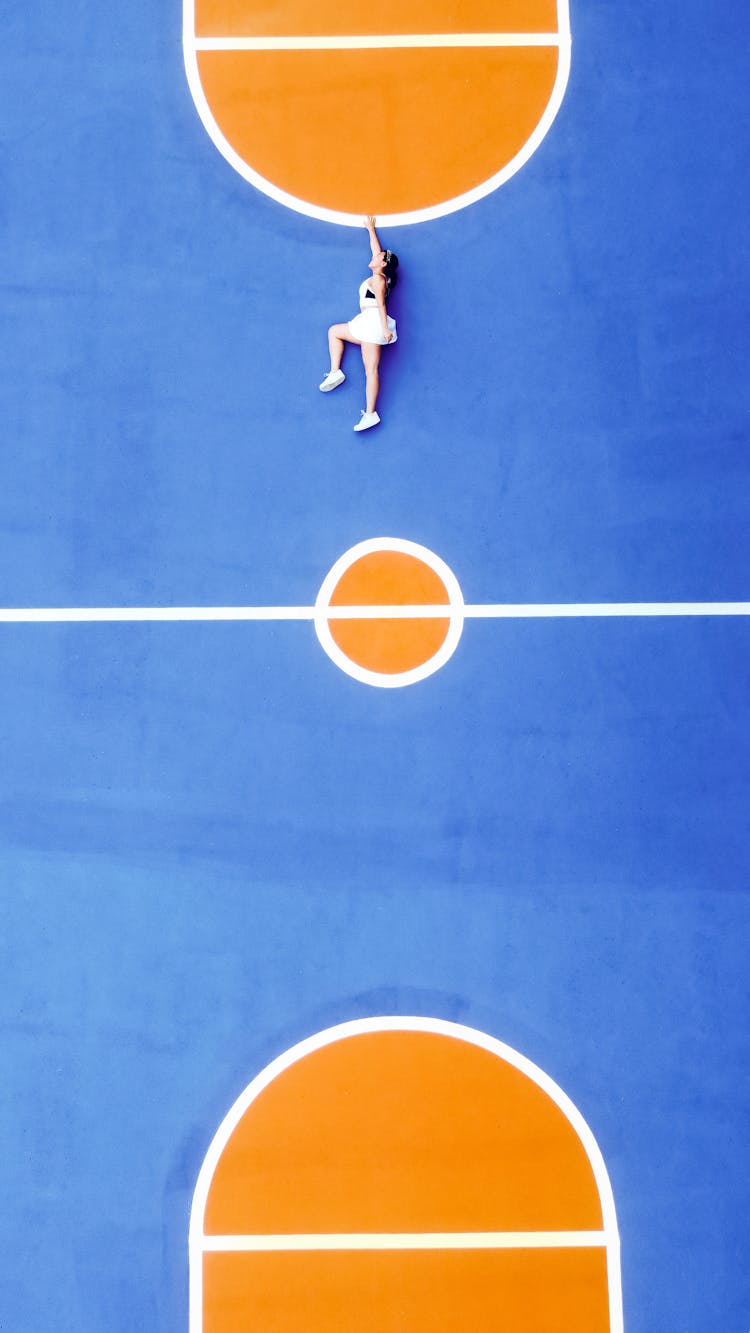 Woman In Sportswear And Sneakers Lying On Blue Sport Ground