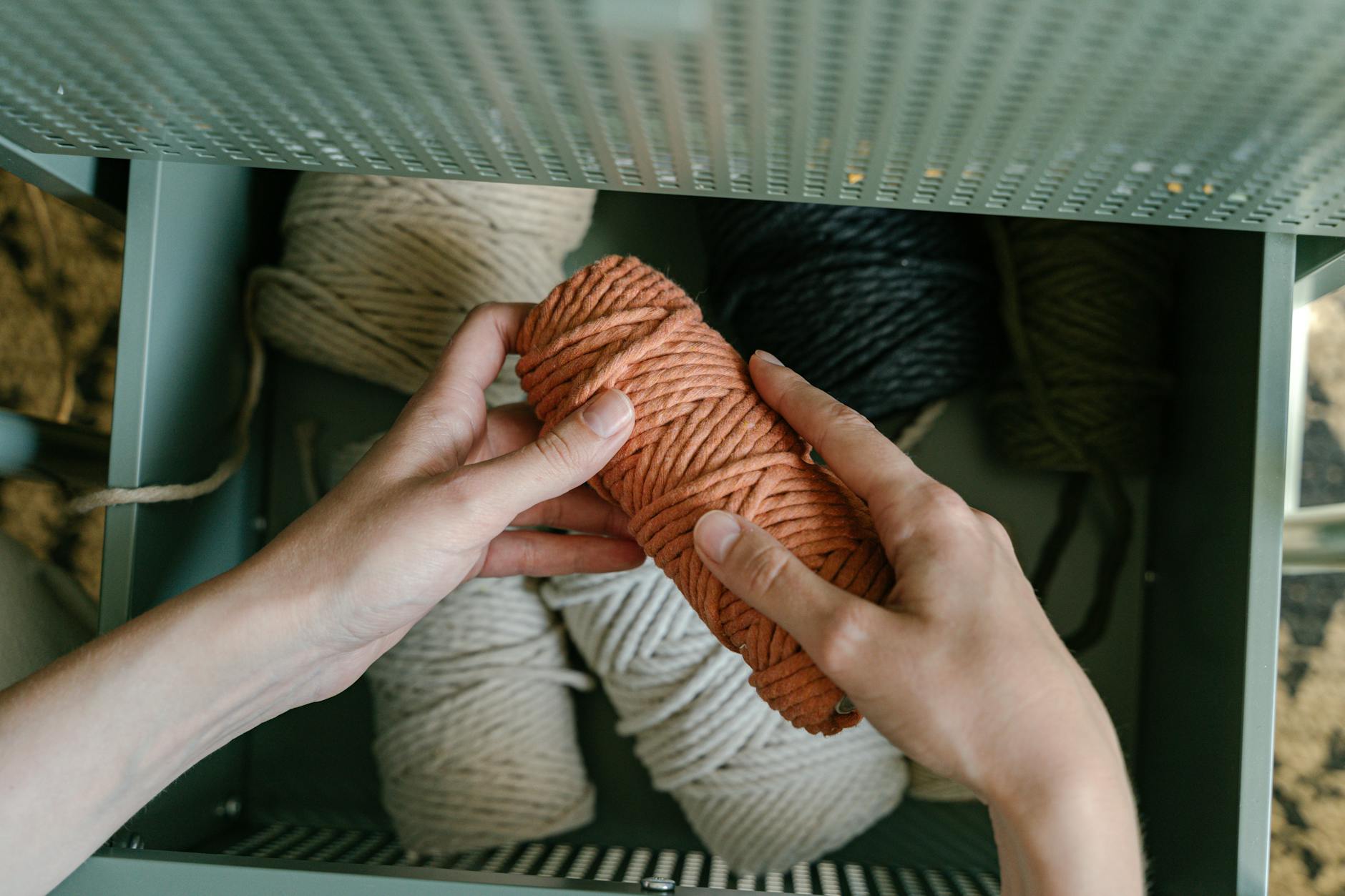 Hands sorting colorful yarn balls in a metal drawer for crafting projects.
