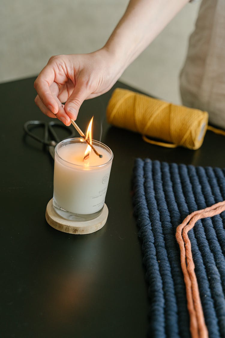 A Hand Lighting A Candle On A Black Table Using A Matchstick