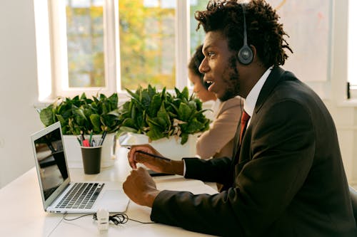 Man in Black Suit Sitting in front of His Laptop while Looking Afar