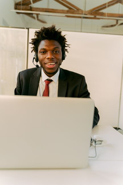 Young man in call center wearing a headset and smiling while working on a laptop in the office.