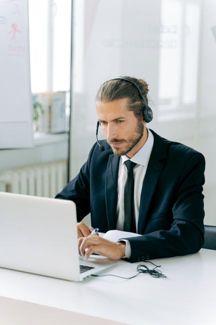Focused customer service agent working at a desk with a headset and laptop in an office setting. Focused customer service agent working at a desk with a headset and laptop in an office setting.