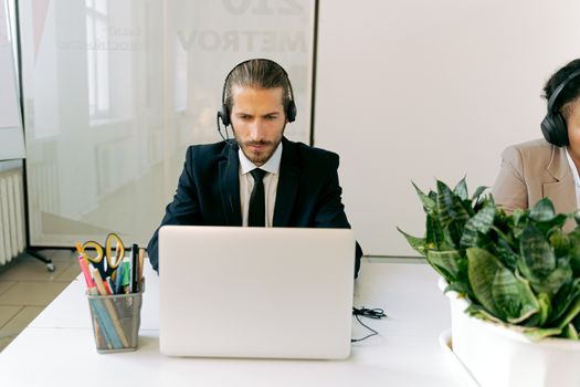 Focused customer support agent using laptop and headset in a modern office setting with greenery.