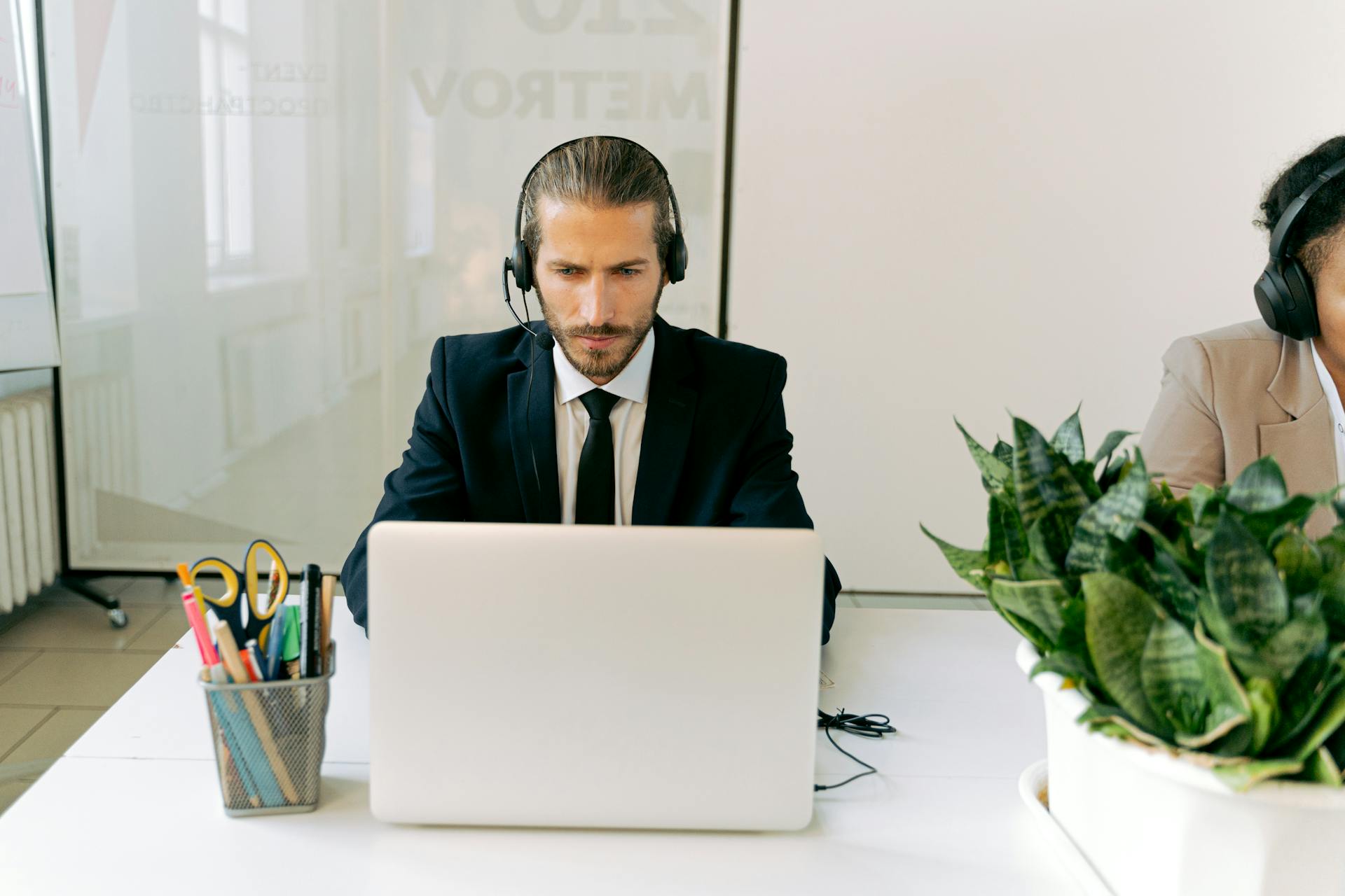 Focused customer support agent using laptop and headset in a modern office setting with greenery.