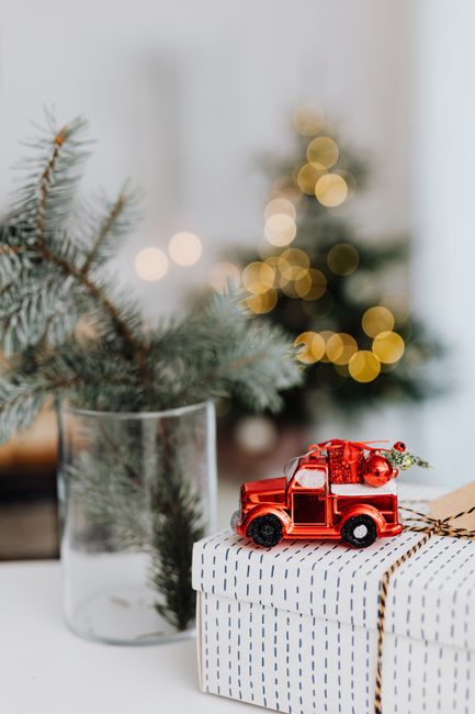 Close-up of a Christmas gift with a red toy car decoration and pine branches, creating a festive holiday atmosphere.