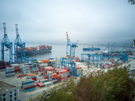 Aerial view of bustling Valparaíso port with container ships and cranes on a foggy day.