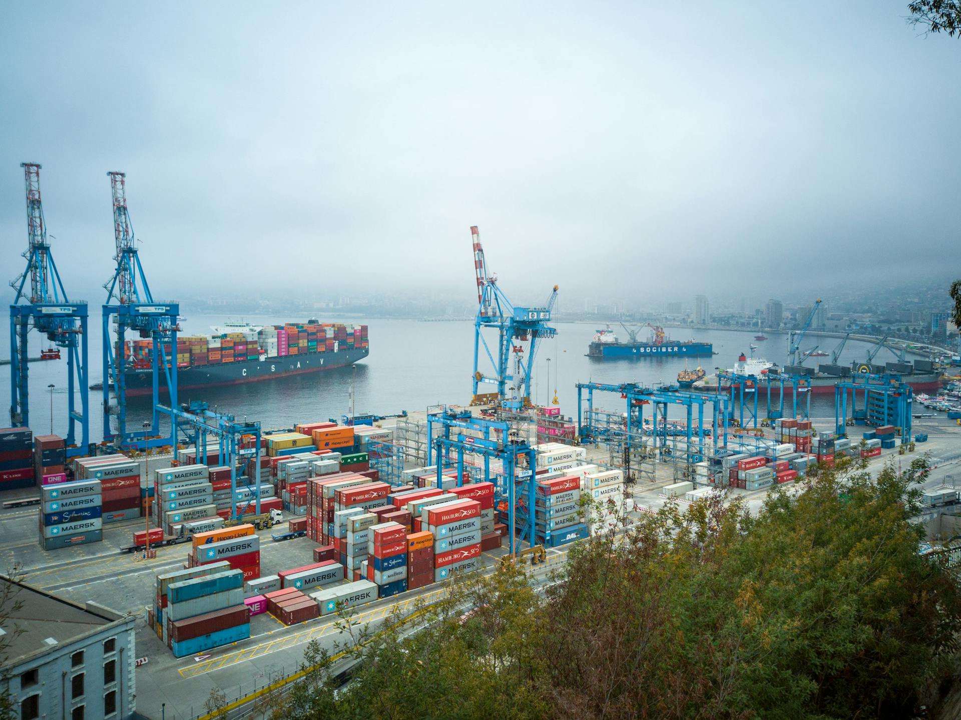 Aerial view of bustling Valparaíso port with container ships and cranes on a foggy day.