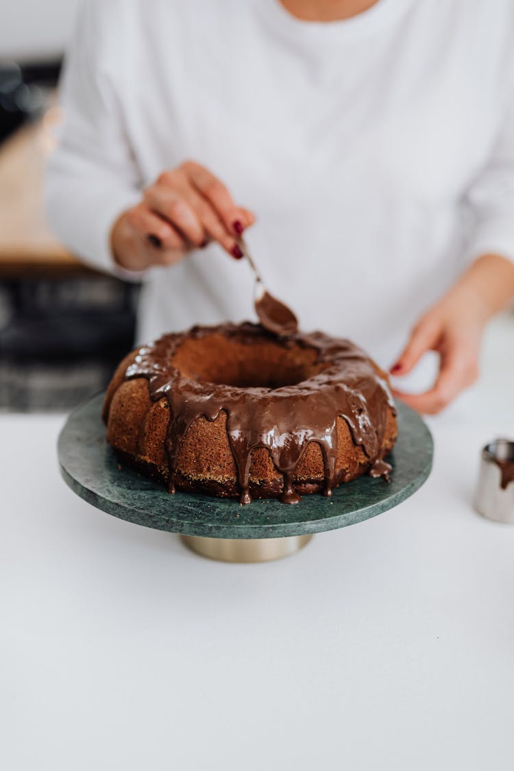 Woman Pouring Chocolate Icing On A Chocolate Sand Cake 