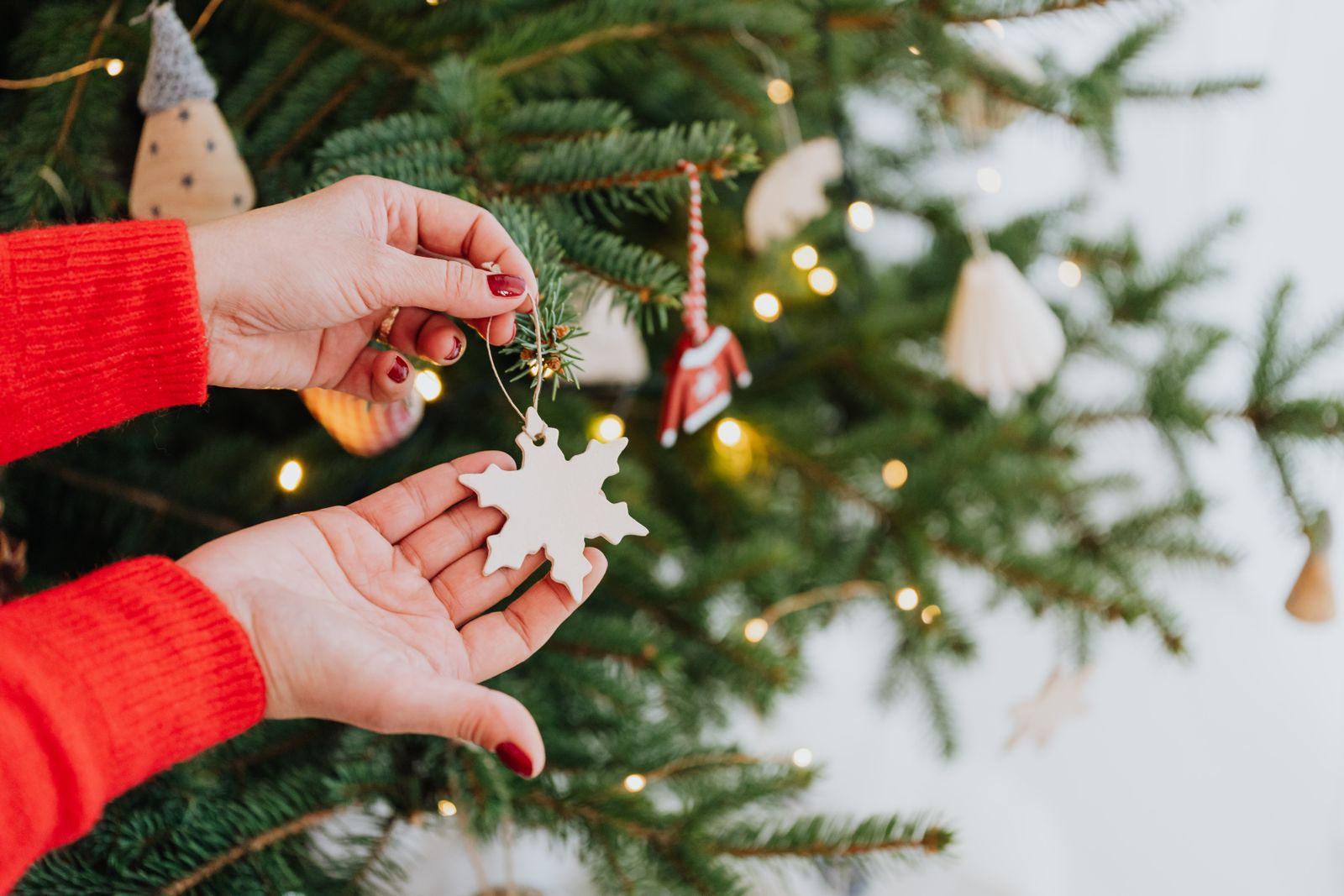 Hand placing a white snowflake ornament on a Christmas tree.