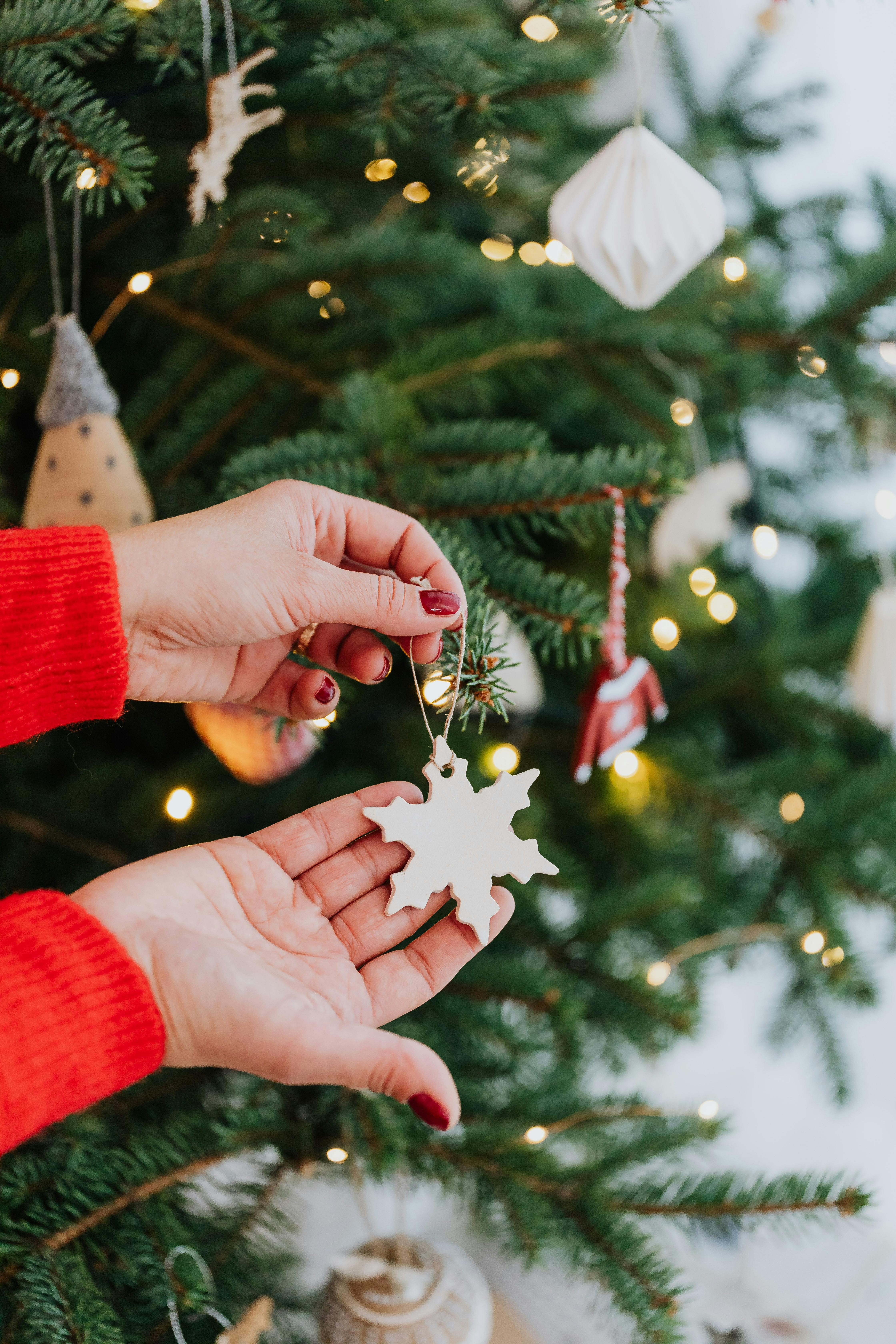 特写镜头聚焦于悬挂圣诞树雪花装饰品的手，烘托出节日的欢庆氛围