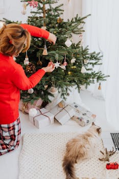 一个女人装饰着圣诞树，她的猫在一旁看着，营造出舒适的节日氛围