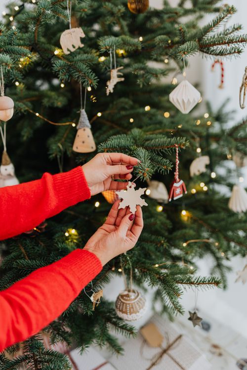 Free Hands decorating a Christmas tree with a snowflake ornament, capturing a festive holiday spirit. Stock Photo