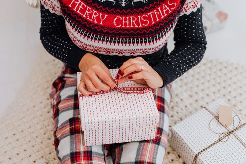 Free Close-up of a woman in a festive sweater wrapping Christmas presents on a cozy knit blanket. Stock Photo