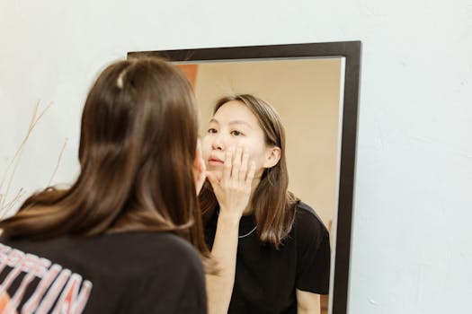 A woman in a black shirt checking her skin in front of a mirror indoors.