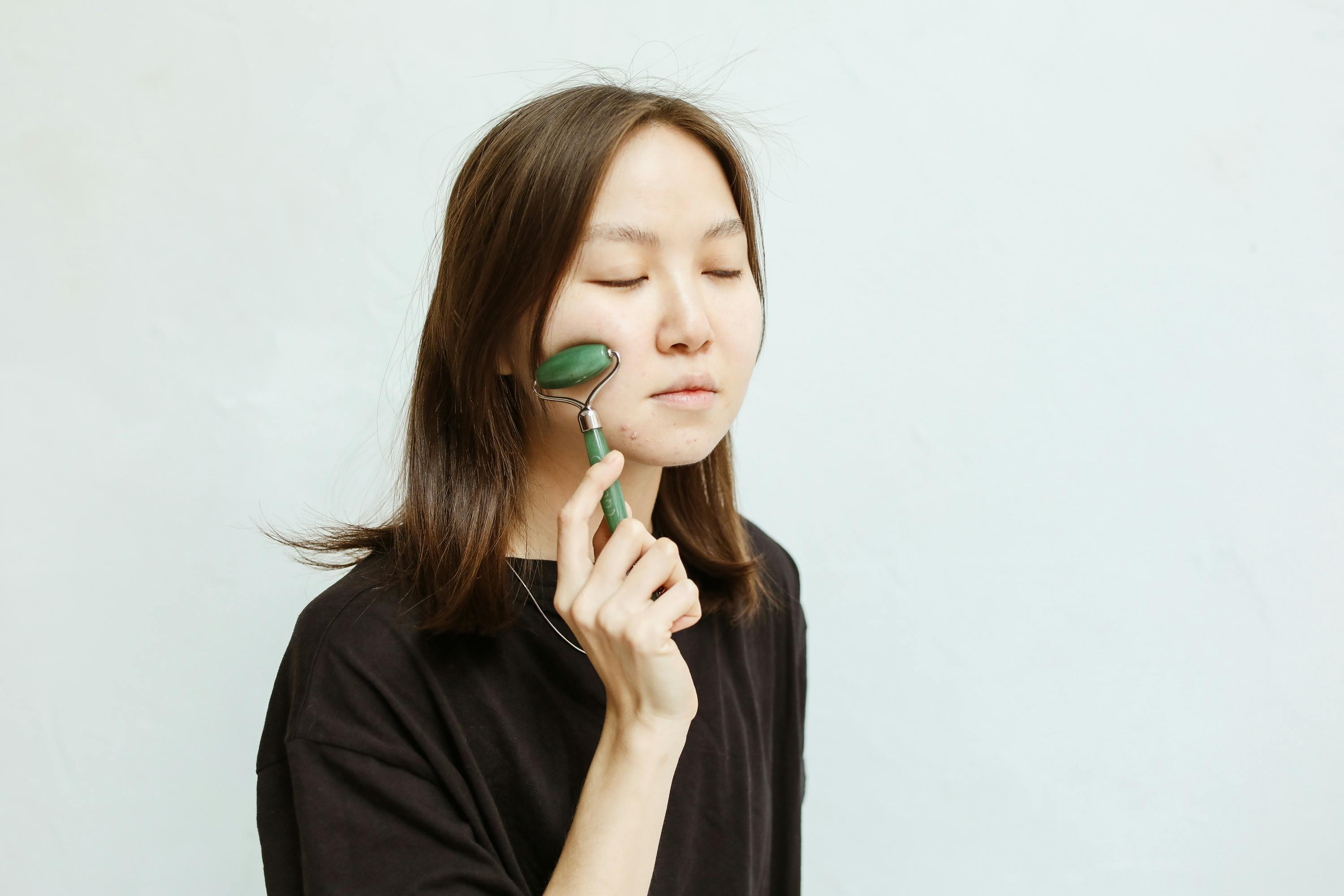 A young woman uses a jade roller in a beauty routine for facial massage and skincare.