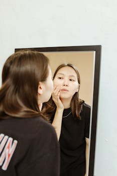 Young woman examines her skin in a mirror for a daily beauty routine.