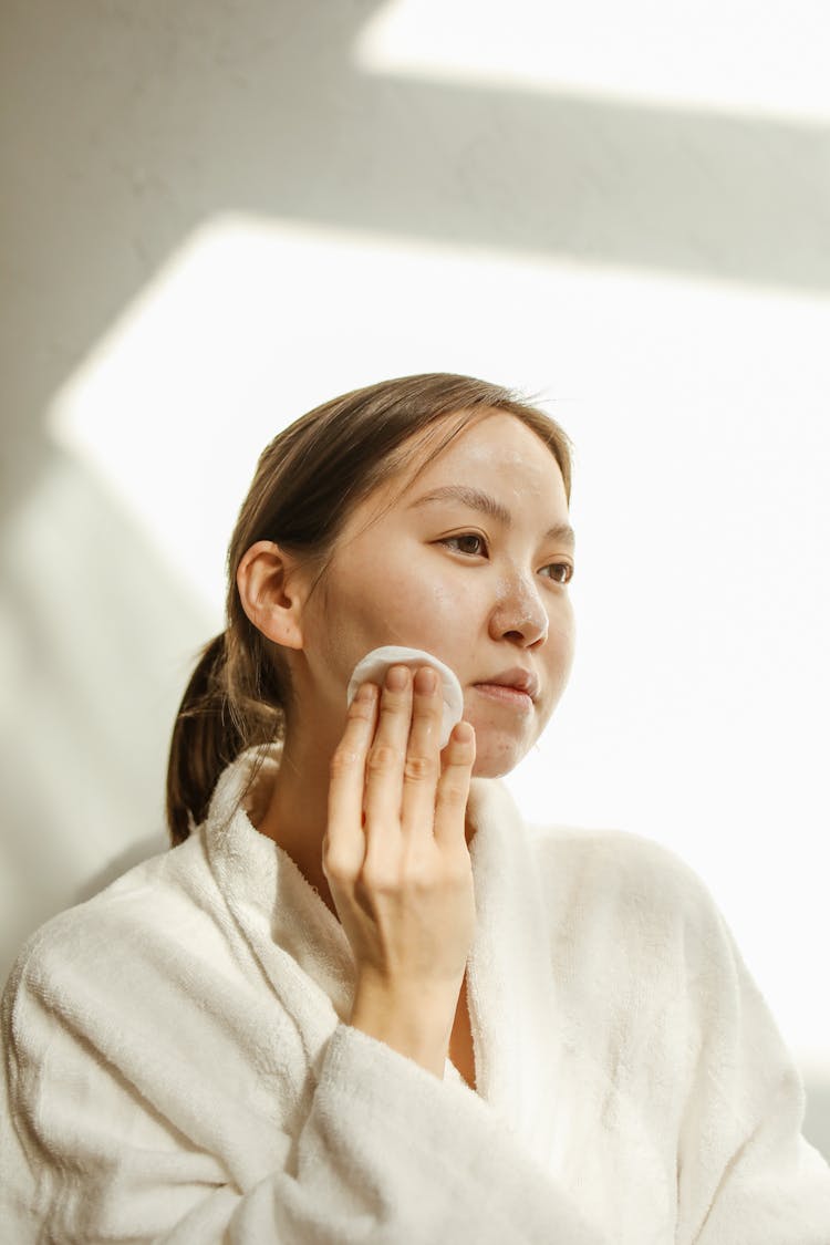 A Woman Wiping Her Face With A Cotton Pad