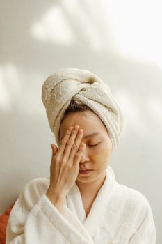 Asian woman applying facial cream during skincare routine, promoting beauty care and relaxation.