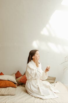 Asian woman in a cozy bedroom applying facial cream, embracing beauty and relaxation.
