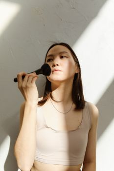 Portrait of a young woman using a makeup brush in soft natural light for beauty routine.