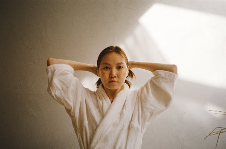 A Woman Wearing A Bathrobe Tying Her Hair