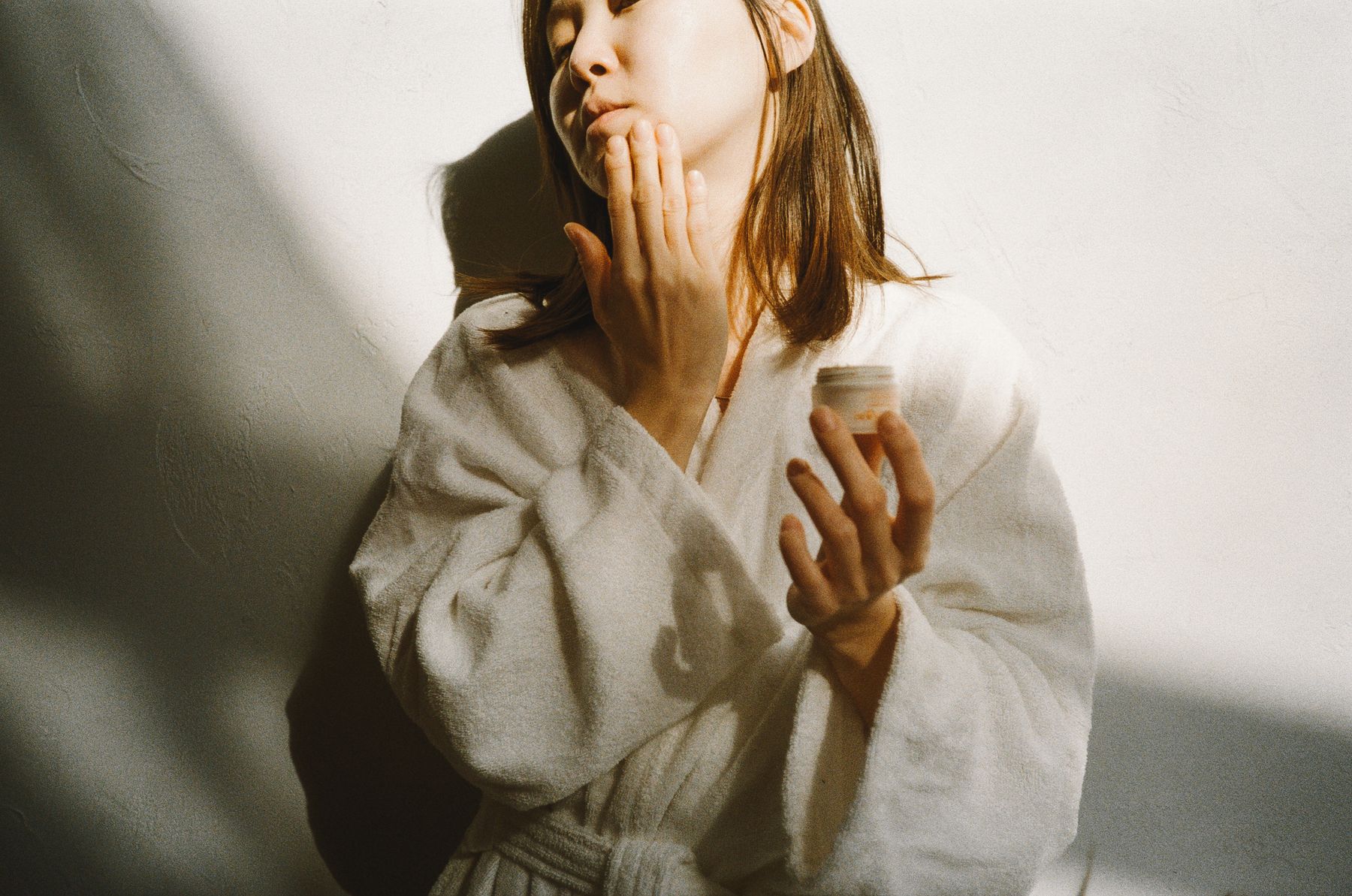 A woman in a robe gently applying face cream in soft morning light