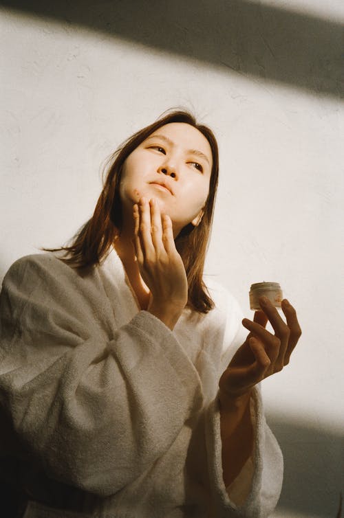 Woman in Applying Moisturizer on Her Face while Looking Afar