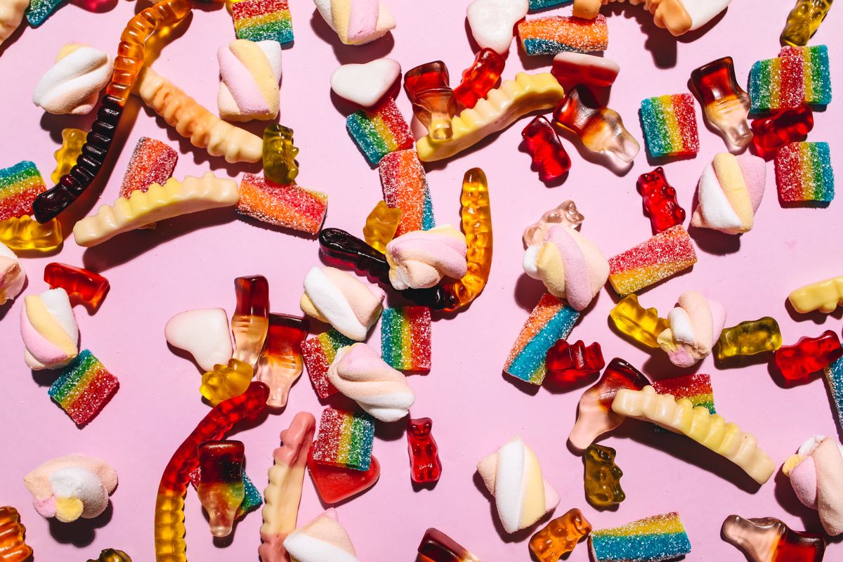 Colourful gummy sweets in assorted shapes arranged on a pink background