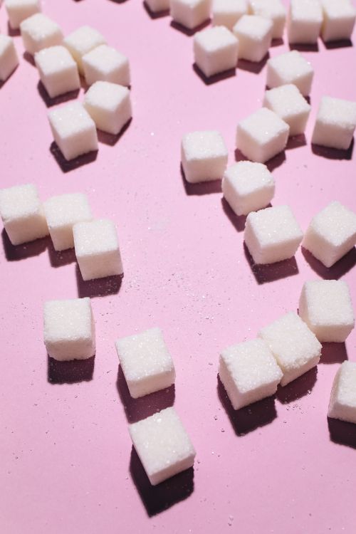 Free Close-up of sugar cubes scattered on a pink background with strong studio lighting. Stock Photo