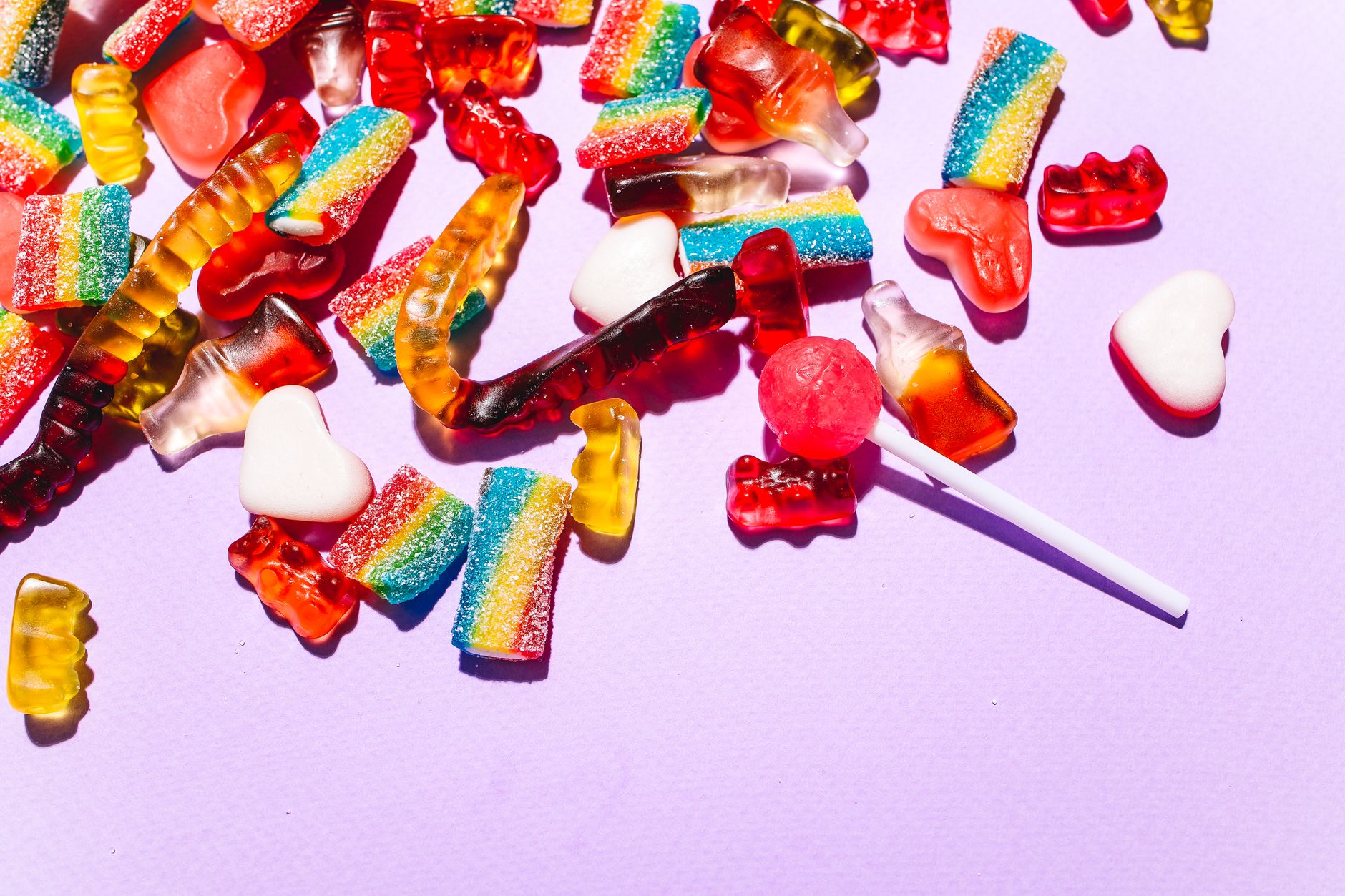 A vibrant mix of gummy candies and lollipops on a lilac background.