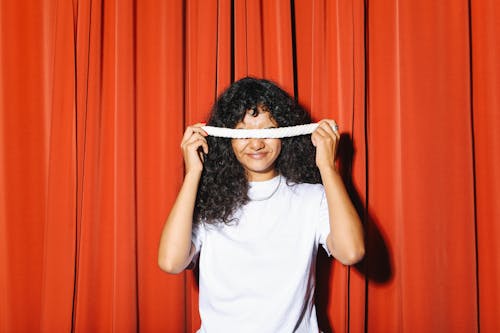 Woman in White Shirt Standing in Front of Red Curtain Holding a Marshmallow