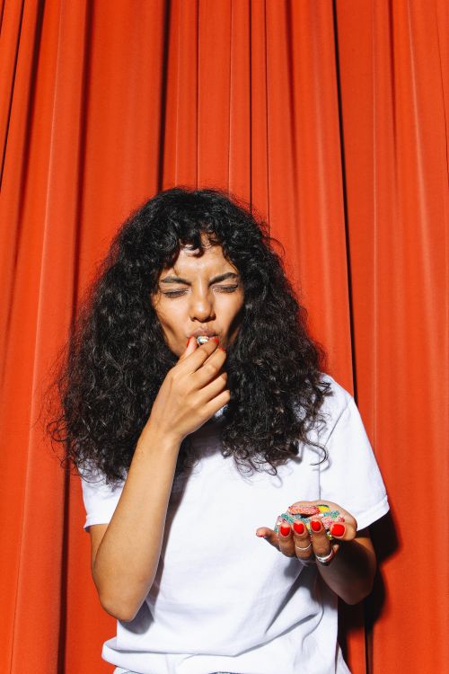 Free Portrait of a woman enjoying colorful candies with playful expression against a red curtain backdrop. Stock Photo