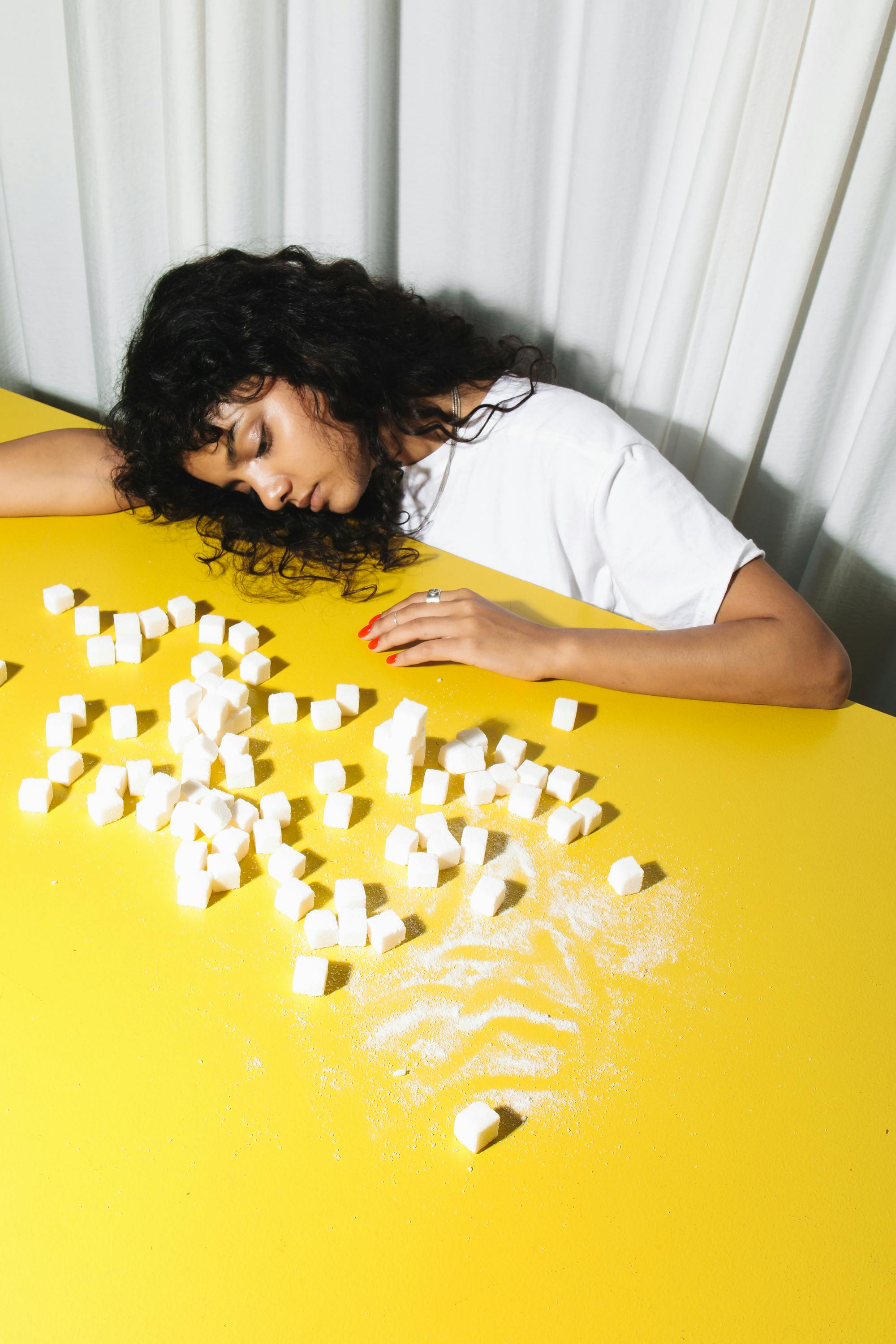 Woman resting on a table with sugar cubes, symbolizing sweet dreams or fatigue.