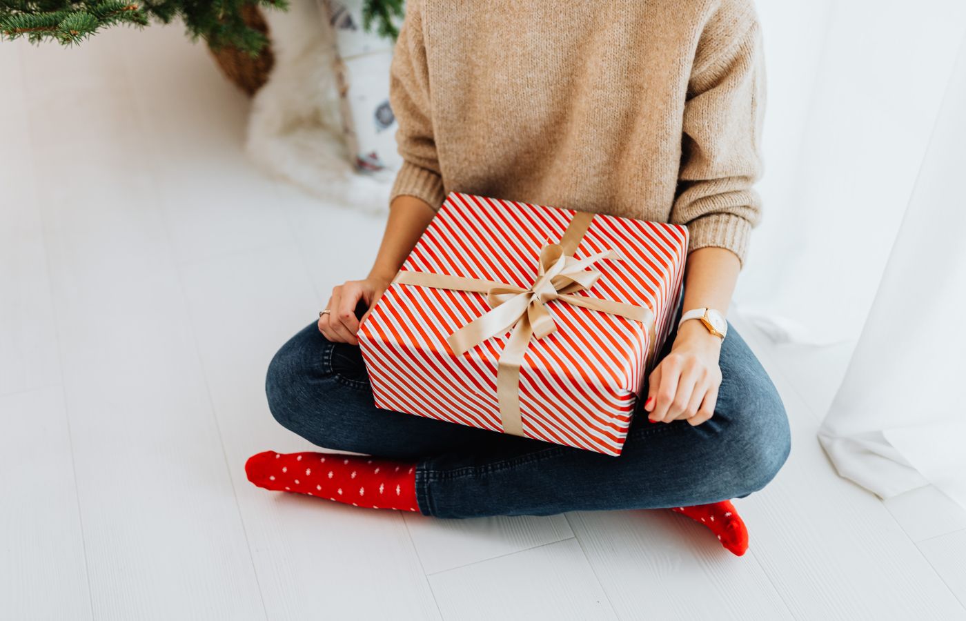 A woman in festive attire holds a beautifully wrapped Christmas gift indoors.