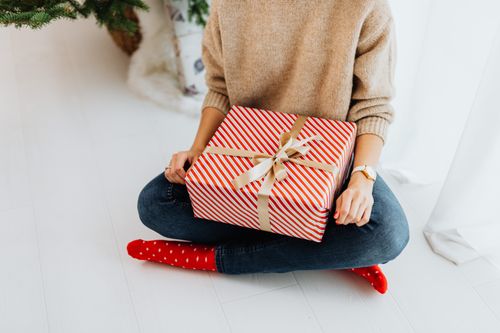 Free A woman in festive attire holds a beautifully wrapped Christmas gift indoors. Stock Photo